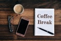 Phone, glasses, coffe mug and notebook with COFFEE BREAK word on wooden table