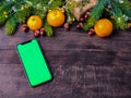Phone with a green chromakey screen on a wooden background with Christmas decor