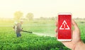 Phone in hand displaying a warning against background of a farmer with a mist sprayer fogger on a farm field. Use of dangerous Royalty Free Stock Photo