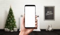 Phone in hand mockup. Christmas scene with decorated Christmas tree, fireplace and poster in background Royalty Free Stock Photo