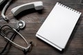 Phone handset, phonendoscope and notebook on dark wooden desk top view call doctor mock up