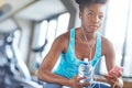 Phone, headphones and black woman in gym with water, fitness app or playlist for music. Health, wellness and girl check Royalty Free Stock Photo