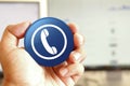 Phone icon blue round button holding by hand infront of workspace background