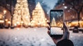phone in man hand making photo of festive colorful Christmas tree and snowman in winter snowy city Royalty Free Stock Photo