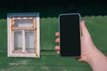 Phone in a man`s hand. Against the backdrop of a house with an old retro wooden window Royalty Free Stock Photo