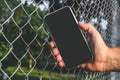 The phone is in the man`s hand. Against the background of a steel wire fence and nature Royalty Free Stock Photo