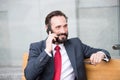 On the phone. Portrait of modern businessman talking on smart-phone while sitting on bench outdoors. bearded man holding glasses Royalty Free Stock Photo