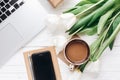 Phone screen and laptop with morning coffee and tulips on white Royalty Free Stock Photo