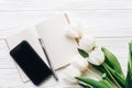 Phone screen and notebook pen and stylish tulips on white wooden Royalty Free Stock Photo