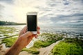The phone is a smartphone in the hand of a man with an empty black screen on the background of the ocean shore and sunlight.