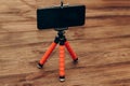 The phone stands on a manual monopod tripod for the camera on a wooden table.