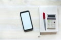 The phone is on the table. Calculator pen and notepad. On a wooden background