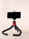 A black phone tripod with flexible legs stands on a light pink background.