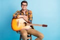 Photo of adorable cute guy dressed plaid shirt spectacles smiling siting chair holding guitar empty space isolated blue Royalty Free Stock Photo