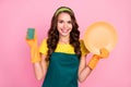 Photo of adorable cute young woman wear green apron rubber gloves smiling washing dishes isolated pink color background Royalty Free Stock Photo