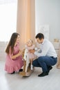 Photo of adorable family woman and man with little girl smiling in children`s room. The daughter sits on a horse gurney Royalty Free Stock Photo