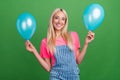 Photo of adorable lady hold two air balloons have fun enjoy event wear striped overall isolated green color background Royalty Free Stock Photo