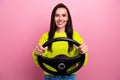 Photo of adorable pleasant girl with brunette hair dressed yellow sweater holding streering wheel isolated on pink color Royalty Free Stock Photo