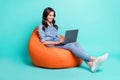 Photo of adorable pretty young lady dressed denim shirt sitting beanbag typing modern gadget isolated teal color Royalty Free Stock Photo