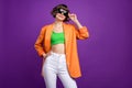 Photo of adorable shiny young woman dressed orange blazer arm dark glasses empty space smiling isolated purple color