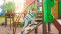 Photo of adorable toddler boy climbing and crawling on wooden staircase on children palyground at park