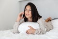 Photo of adorable woman 30s using mobile phone, while lying in bed with white linen in bright room Royalty Free Stock Photo