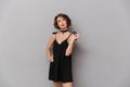 Photo of adorable woman 20s wearing black dress smiling at camera, isolated over gray background