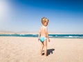 Image of adorable 3 years old little boy walking on the hot beach sand to the sea. Child relaxing and having good time Royalty Free Stock Photo