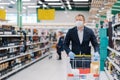 Photo of adult man wears disposable face mask, makes shopping, thinks about protection and prevent measures during coronavirus