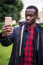 Photo of african happy man holding his cellphone in hands and make a selfie outdoors. Royalty Free Stock Photo