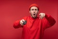 Photo of agitated man wih beard in red clothing pointing fingers at camera holds tv console with surprise and opened