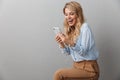 Photo of alluring blond businesswoman with long curly hair smiling while listening to music with smartphone and earphones