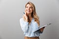 Photo of alluring blond secretary woman with long curly hair thinking and holding clipboard while working in office Royalty Free Stock Photo