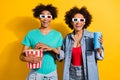 Photo of amazed dark skin people couple relationship movie glasses pop corn drink isolated on yellow color background Royalty Free Stock Photo