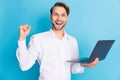 Photo of amazed happy victorious young man raise fist hold laptop winner isolated on blue color background
