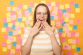 Photo of amazed surprised woman with brown hair in striped t shirt standing against yellow wall with colorful stickers, sees Royalty Free Stock Photo