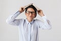 Photo of amusing female worker wearing eyeglasses holding book on head in the office, isolated over white background