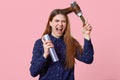 Photo of annoyed young woman combs her hair, dissatisfied with shampoo, holds hairbrush and hairspray, looks with irritated