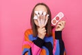 Photo of anonymous funny woman with dark straight hair wearing jumper standing over pink background, covering her face