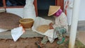 Photo of an Asian farmer sorting rice in front of a wooden house