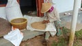 Photo of an Asian farmer sorting rice in front of a wooden house