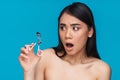 Surprised young woman holding eyelash curler