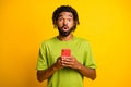 Photo of astonished dark skin guy impressed smartphone blogger novelty isolated on bright yellow color background