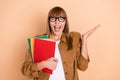 Photo of astonished happy young woman raise hand hold notebooks wear glasses isolated on pastel beige color background