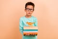 Photo of astonished intelligent charming kid boy hold book learn literature wild animal dinosaurs isolated on beige