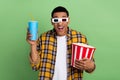 Photo of astonished man hold big popcorn bucket soda drink cup watch movie 3d glasses isolated on green color background Royalty Free Stock Photo