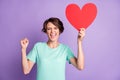 Photo of astonished young lady wear casual teal outfit holding big red heart arm fist closed eyes isolated purple color Royalty Free Stock Photo