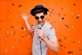 Photo of attractive crazy funky youngster guy singing karaoke using microphone confetti falling wear retro hat sun specs