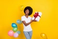 Photo of attractive dark skin jeans happy woman fall balloons hold shake gift isolated on yellow color background