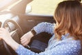 Photo of attractive female checks time on watch, sits in car, stuck in traffic jam and being late for meeting with colleagues, has